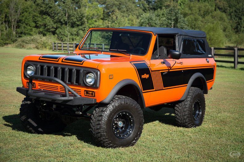 An orange and black jeep is parked in a grassy field.