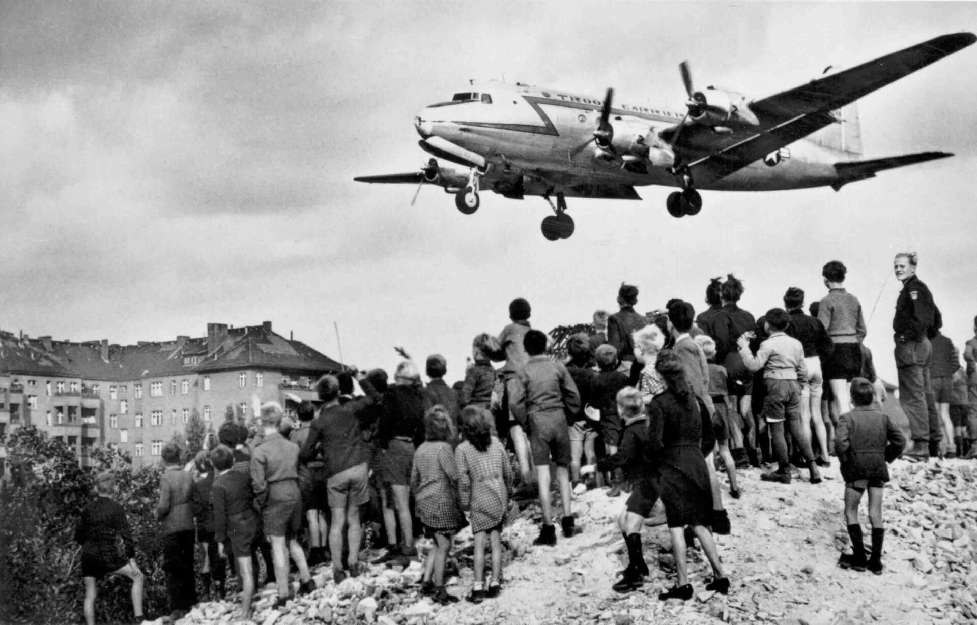 A black and white photo of a plane flying over a crowd of people