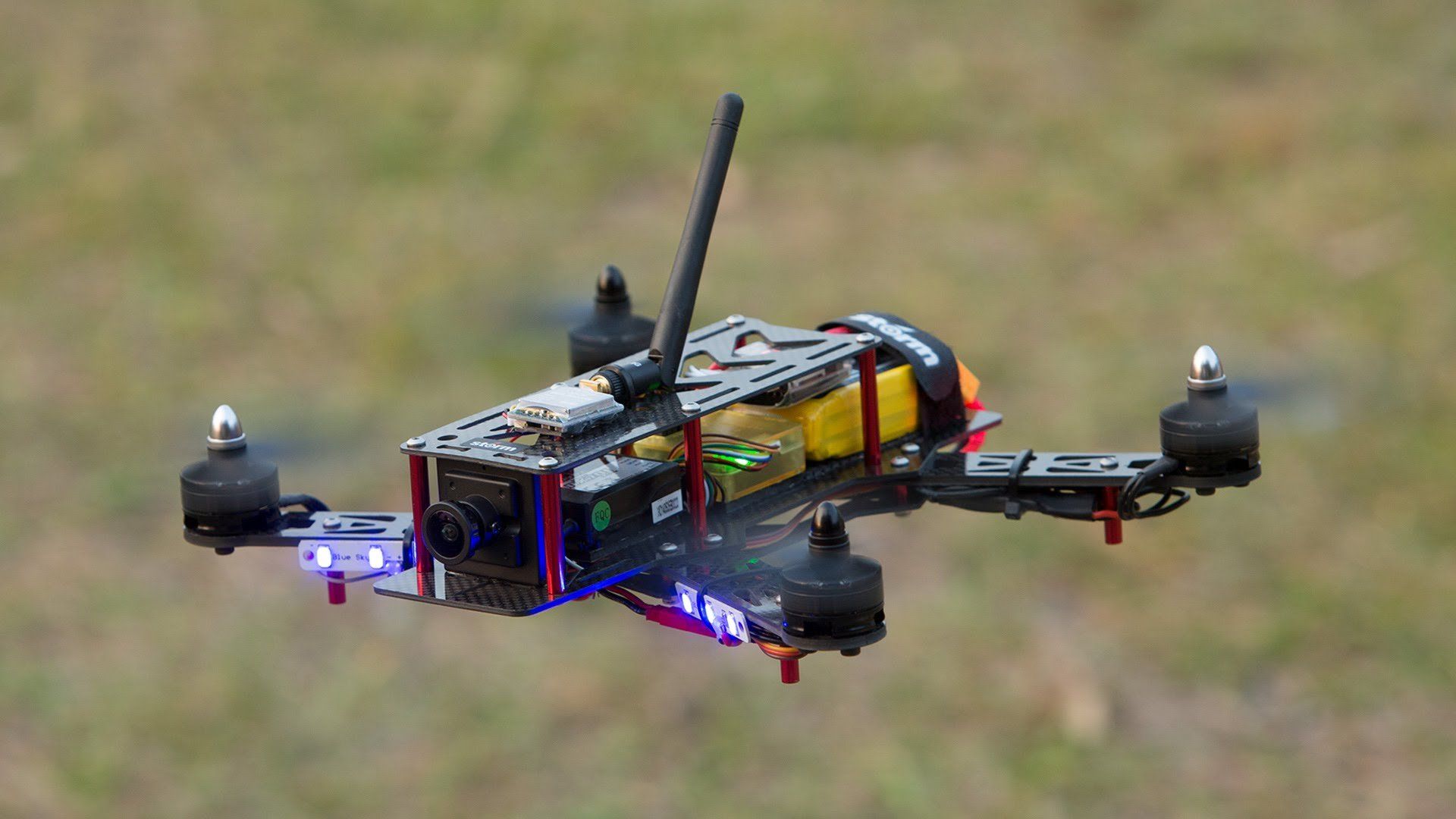 A small drone is flying over a grassy field.