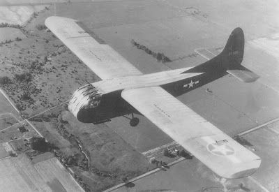 A small plane is flying over a field in a black and white photo.