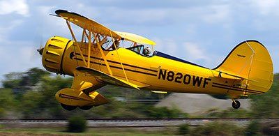 A yellow biplane with the numbers n820wf on the side is flying over a field.