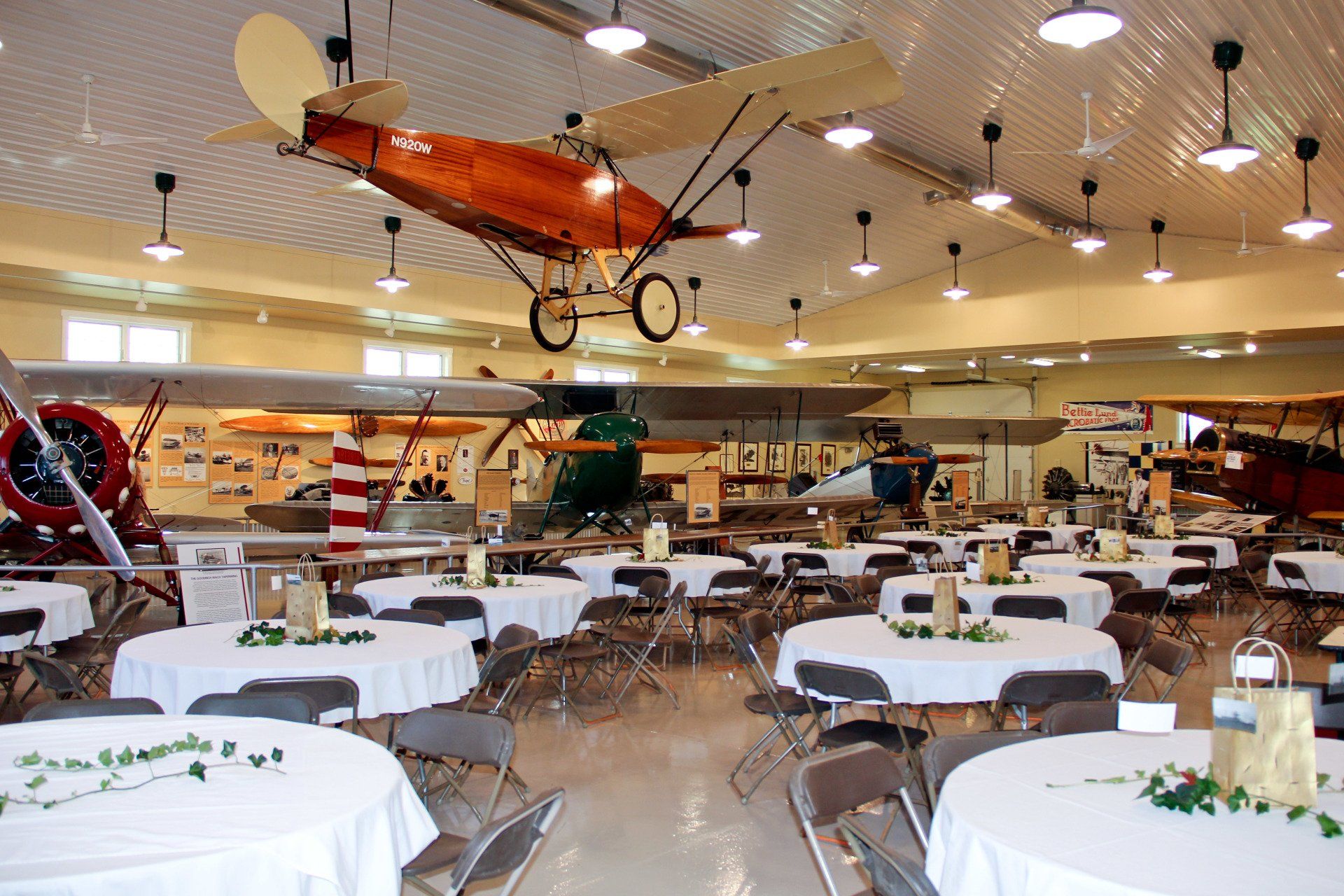 A large room with tables and chairs and a plane hanging from the ceiling
