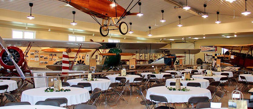 A large room with tables and chairs and a plane hanging from the ceiling.