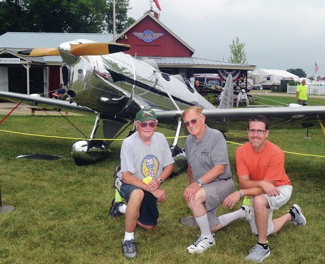 Three men are posing for a picture in front of a small plane