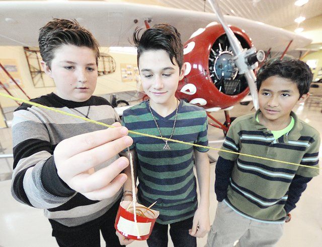 Three young boys are standing in front of an airplane