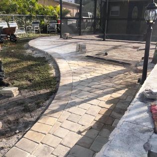 A brick walkway is being built in the backyard of a house