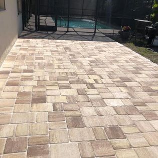 A brick patio with a pool in the background