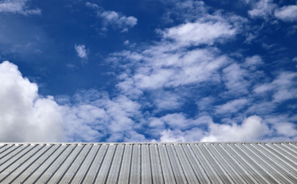 Corrugated metal roof against a vibrant blue sky with white fluffy clouds — JLH Plumbing, Gas & Roofing in South Nowra, NSW