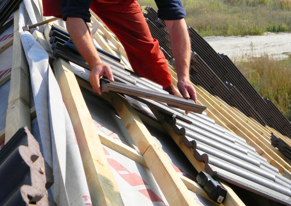 Person Installing Dark Corrugated Roof Tiles on a Wood-framed — JLH Plumbing, Gas & Roofing in South Nowra, NSW