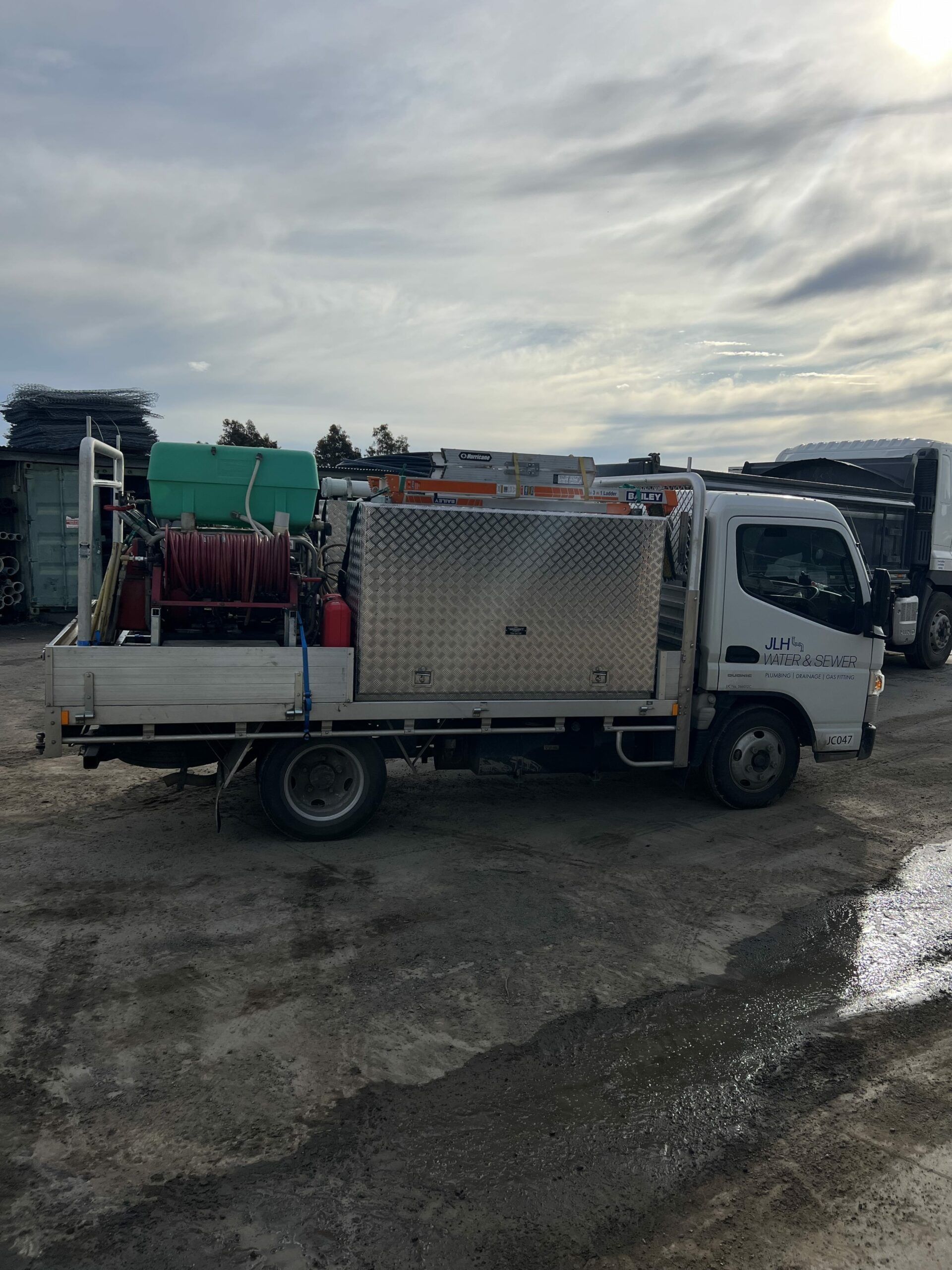 White service truck with large metal storage box and red hose reel parked outside under a cloudy sky — JLH Plumbing, Gas & Roofing in South Nowra, NSW