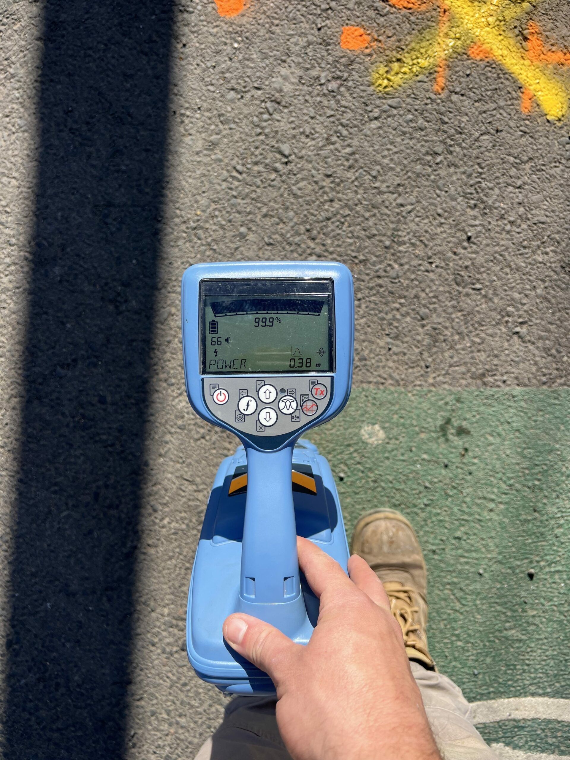 Person holding a blue utility locator, with digital display, on pavement marked with orange and yellow paint — JLH Plumbing, Gas & Roofing in South Nowra, NSW