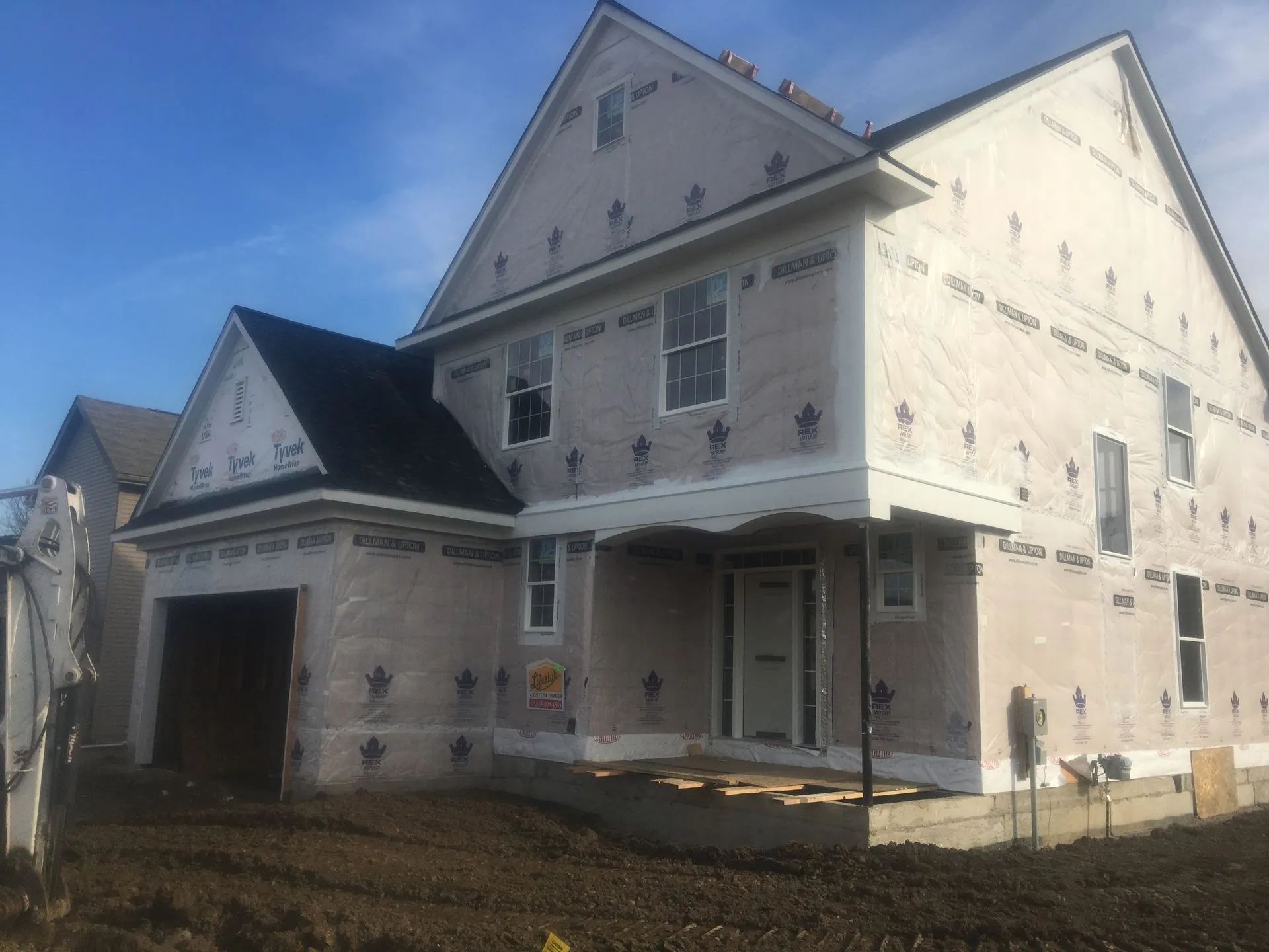 New house under construction, exterior with protective wrap, garage, two stories, sunny day.
