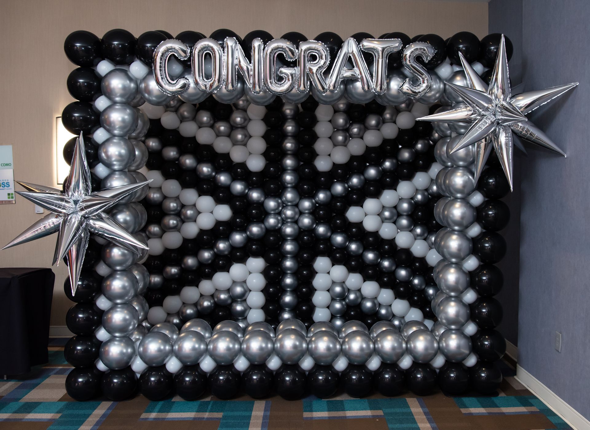 A black and silver balloon wall with the words `` congratulations '' written on it. Graduation balloon wall