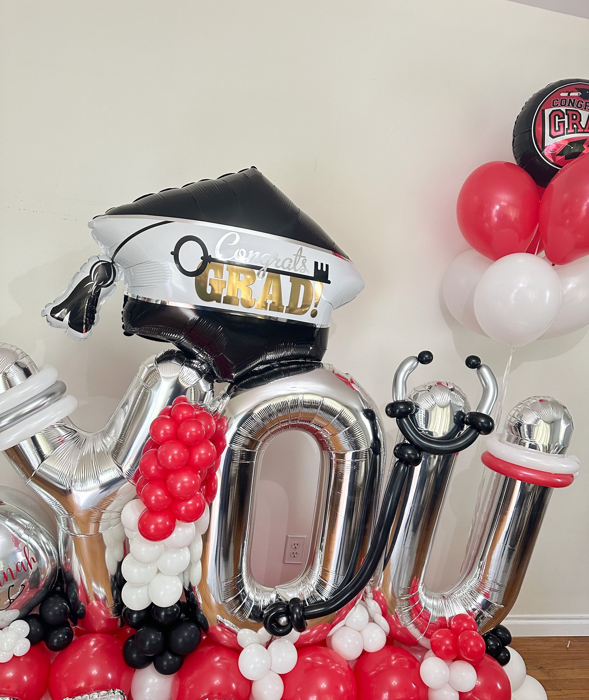 A balloon with a graduation cap on it is surrounded by red and white balloons.