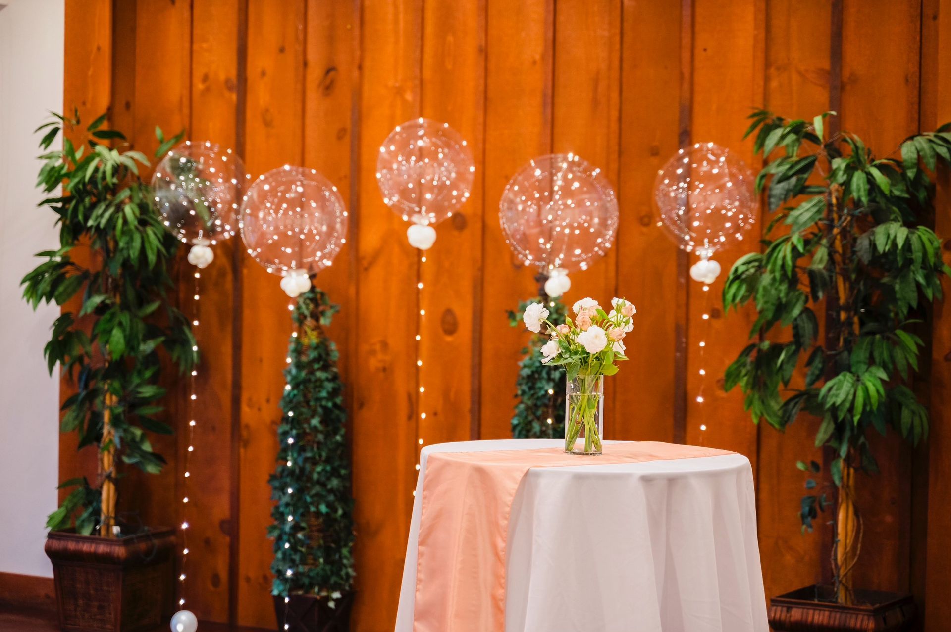 A table with balloons and flowers on it in front of a wooden wall.