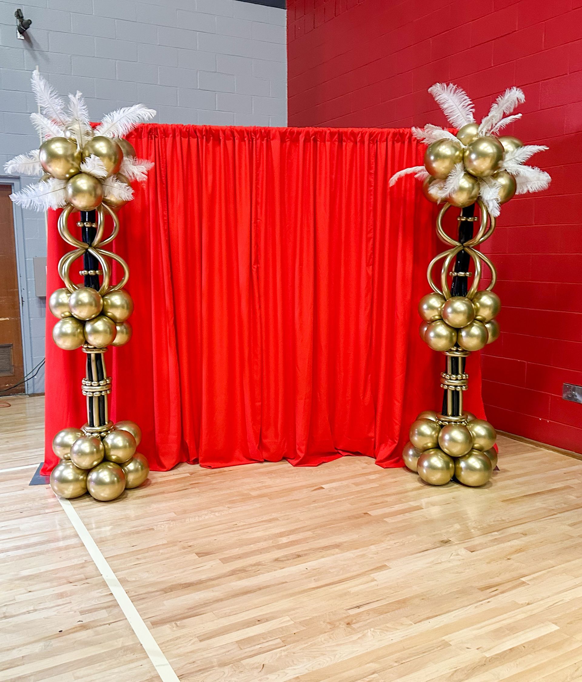 A red curtain is behind two columns of gold balloons.