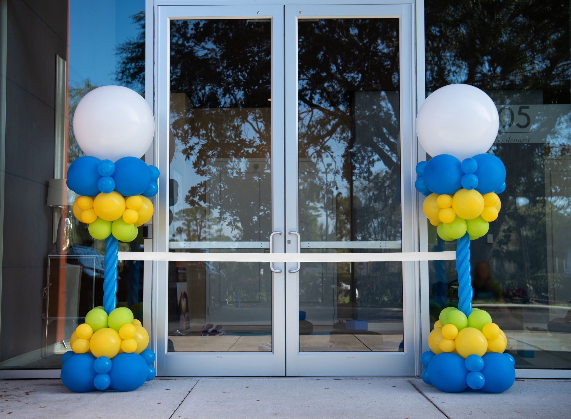Blue yellow and white balloons are lined up in front of a glass door.