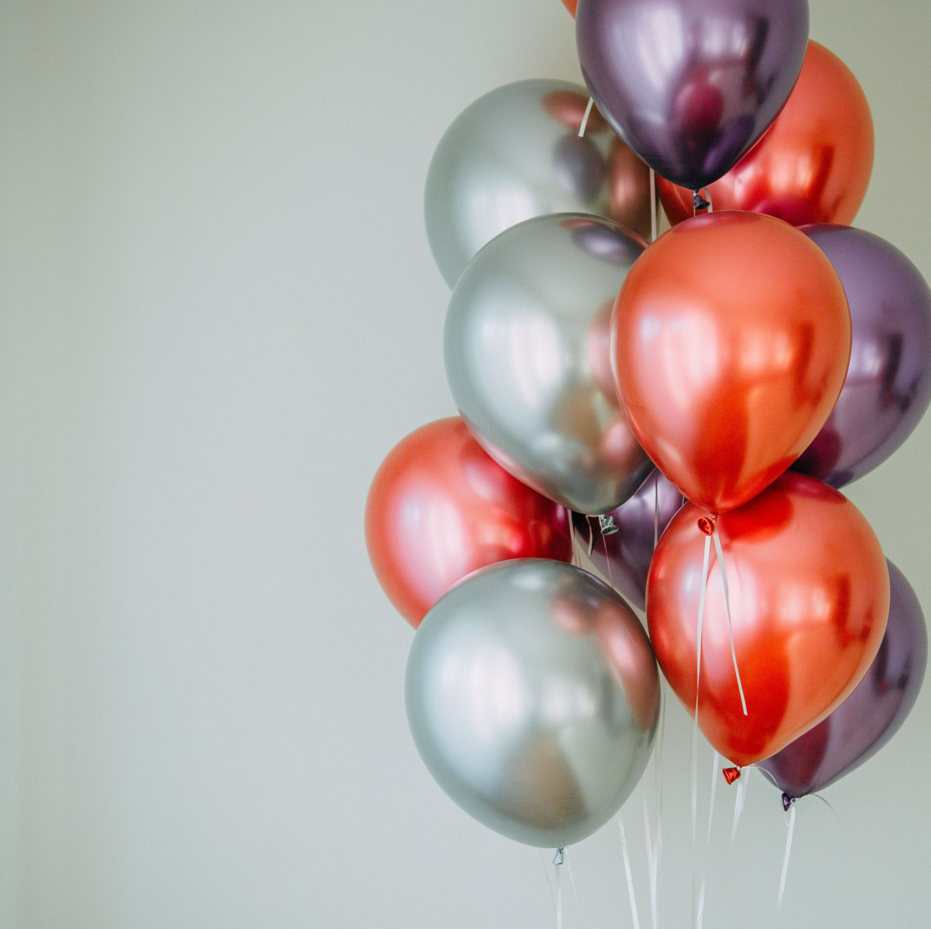 A bunch of red , silver and purple balloons hanging from a string.