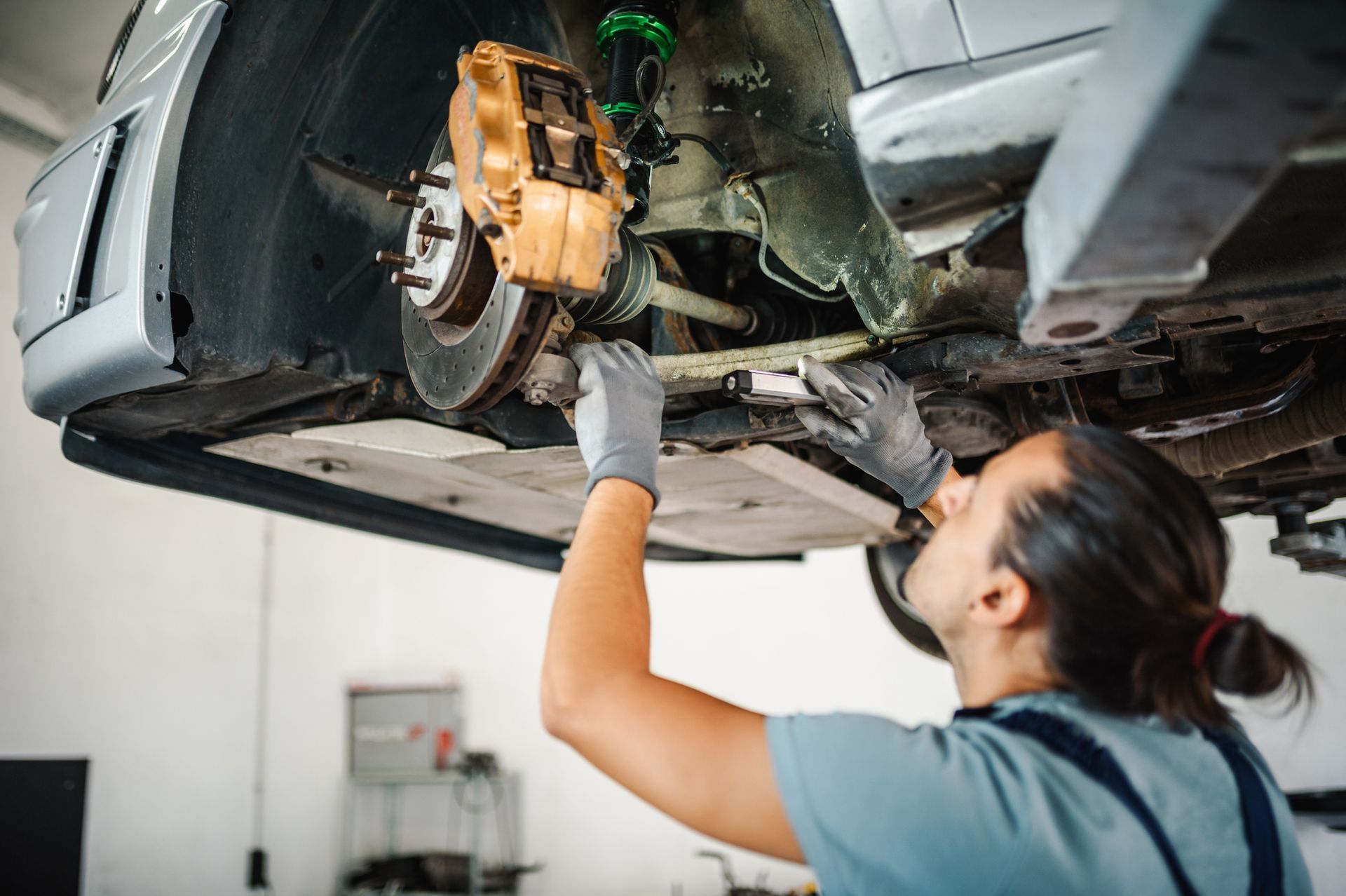 A woman is working on the underside of a car in a garage.