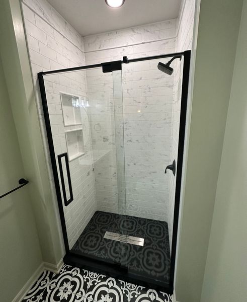 A bathroom with a walk in shower with a black frame.
