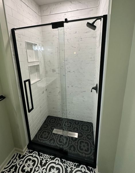 A shower stall with a black frame and sliding glass doors in a bathroom.
