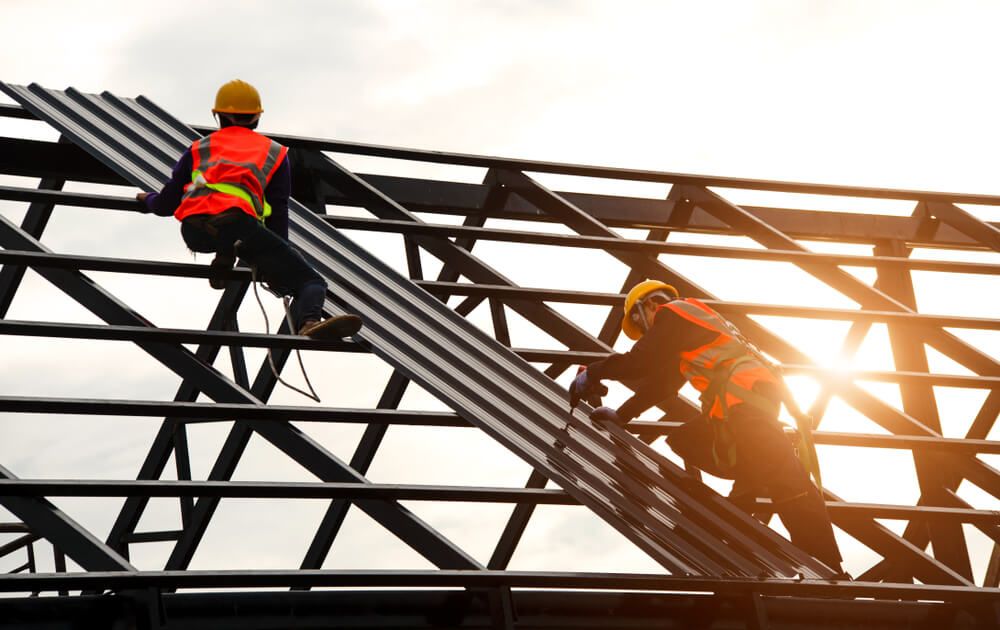 Two construction workers are working on the roof of a building — Fullerton's Plumbing Manufacture In Woree, QLD