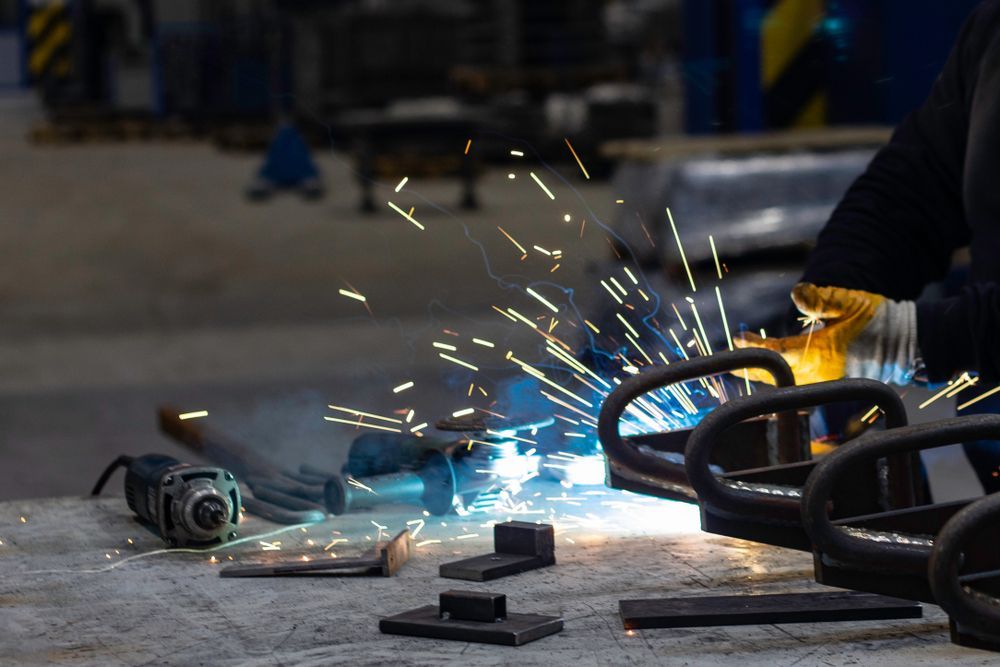 A Man Is Welding A Piece Of Metal In A Factory — Fullerton's Plumbing Manufacture In Woree, QLD
