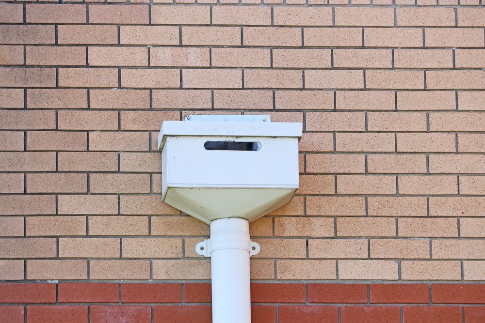 A White Drainpipe Is Attached To A Brick Wall — Fullerton's Plumbing Manufacture In Woree, QLD