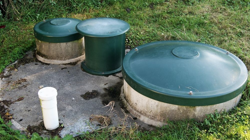 A Septic Tank With Three Green Lids And A White Pipe In The Grass — Fullerton's Plumbing Manufacture In Woree, QLD