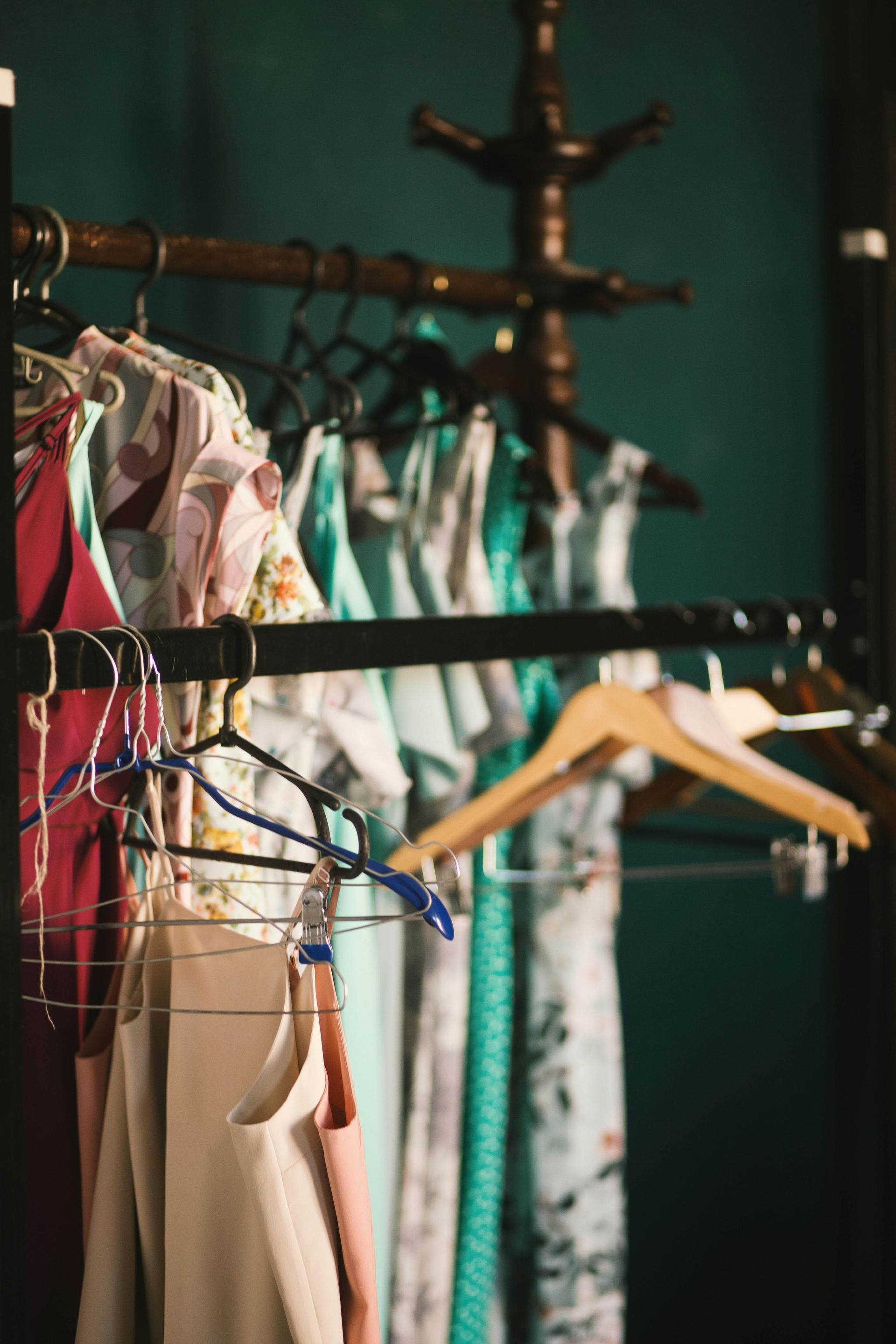 Clothes hanging on a rack in front of a teal wall; various colors and patterns.
