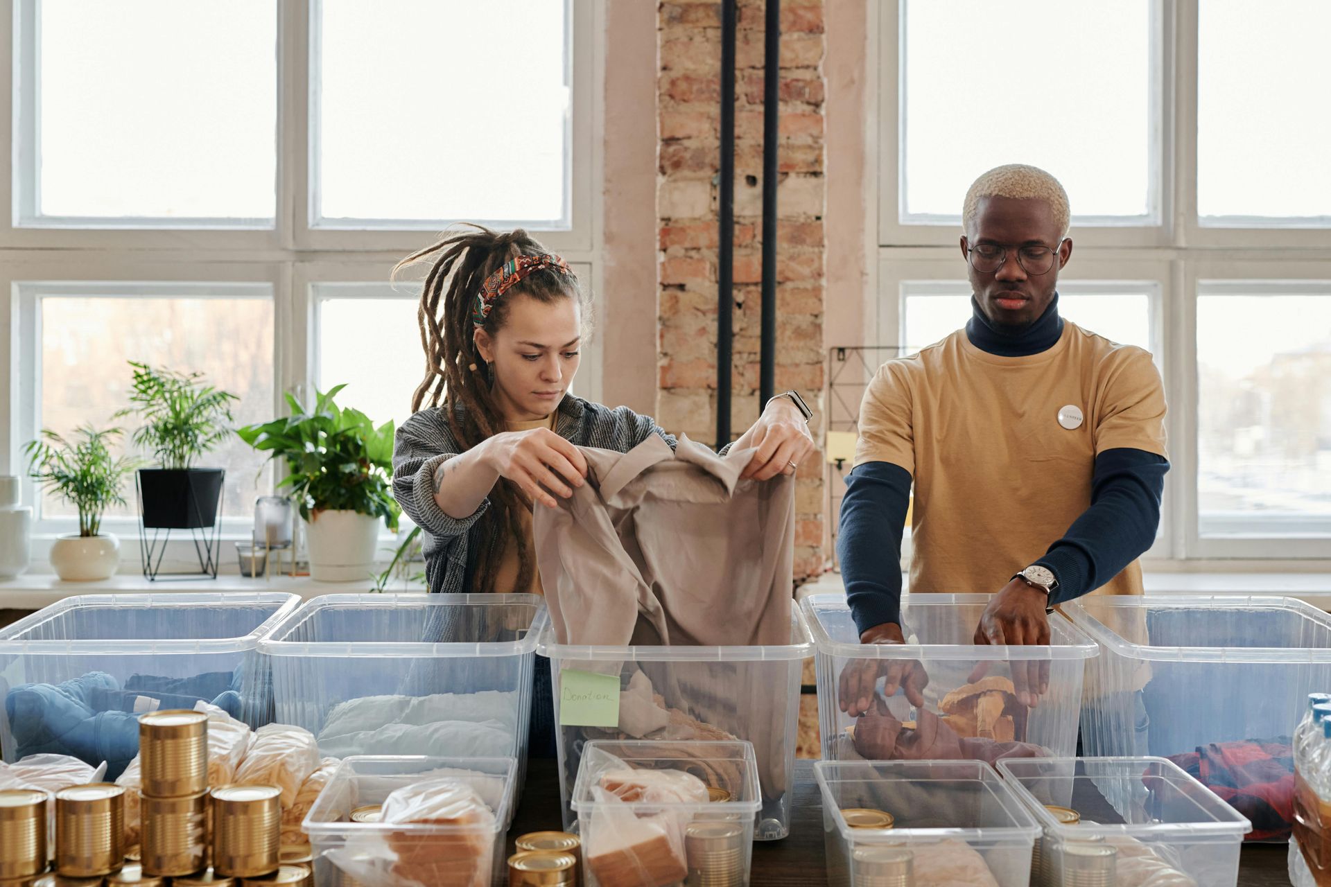 Two people sorting items into clear bins at a bright, well-lit sorting center.