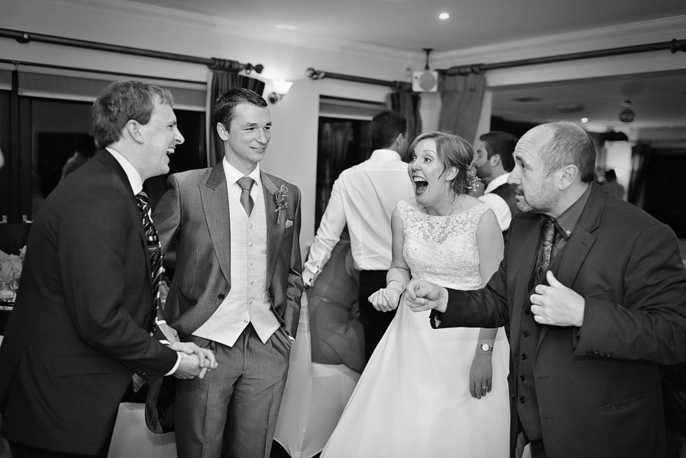 A black and white photo of a bride and groom laughing with their wedding guests.