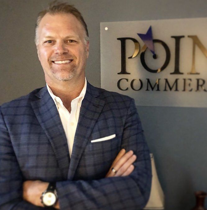 A man in a suit stands in front of a point commer sign