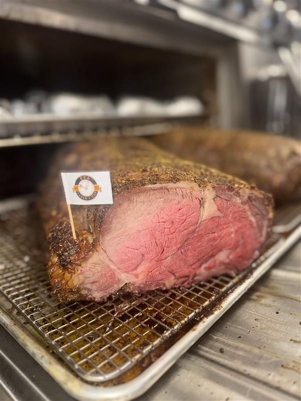 A large, seasoned roast of beef sits on a wire rack inside a kitchen oven, featuring a small white flag marker.