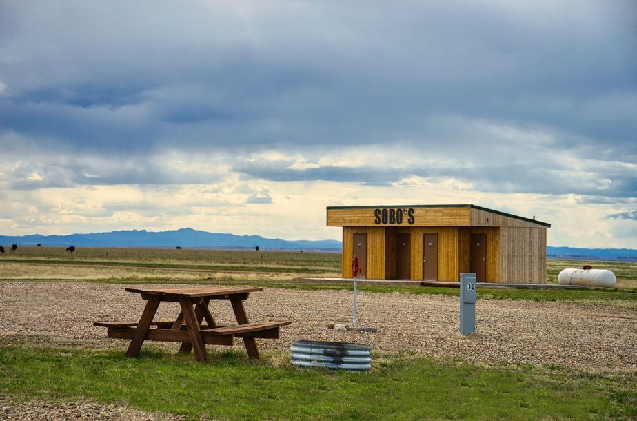 Shower house at Sobos Campground in the Black Hills. Picnic table, RV hookup, and fire pit in the foreground.