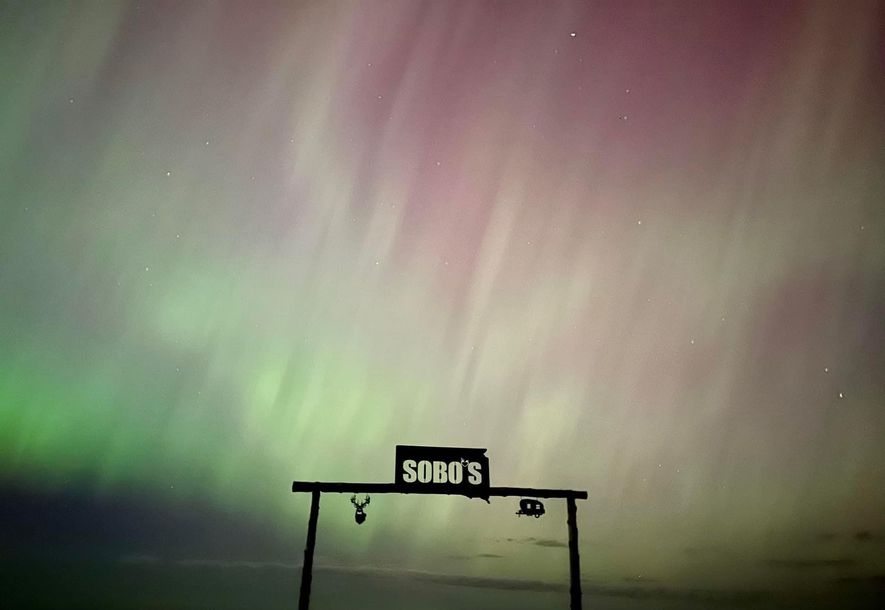 Sobos welcome sign with beautiful green to purple aurora borealis lights behind it.