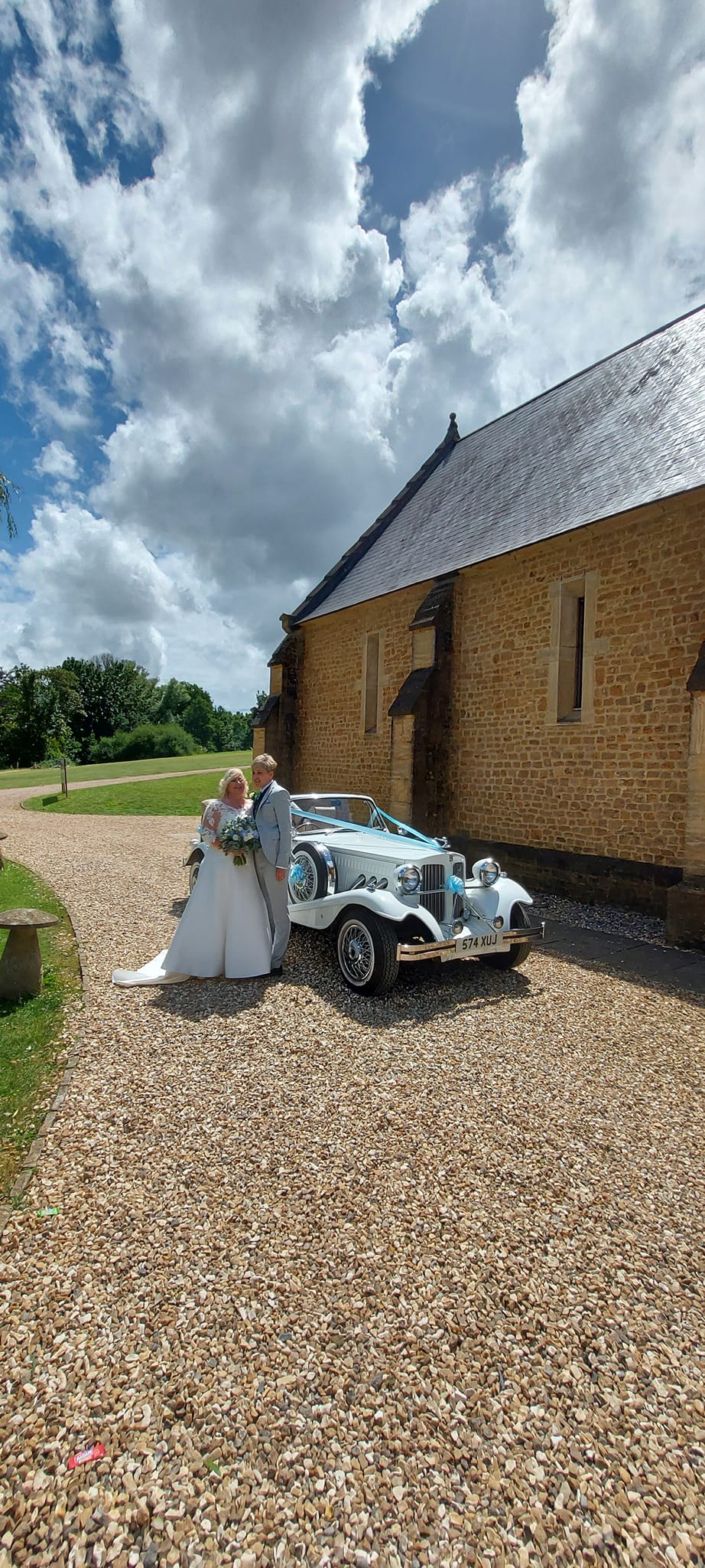 Spirit Wedding Cars | A bride and groom are standing next to a white car in front of a stone building.