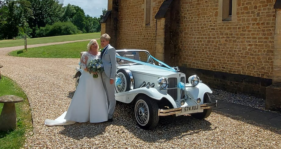 Spirit Wedding Cars | A bride and groom are posing for a picture in front of a wedding car.