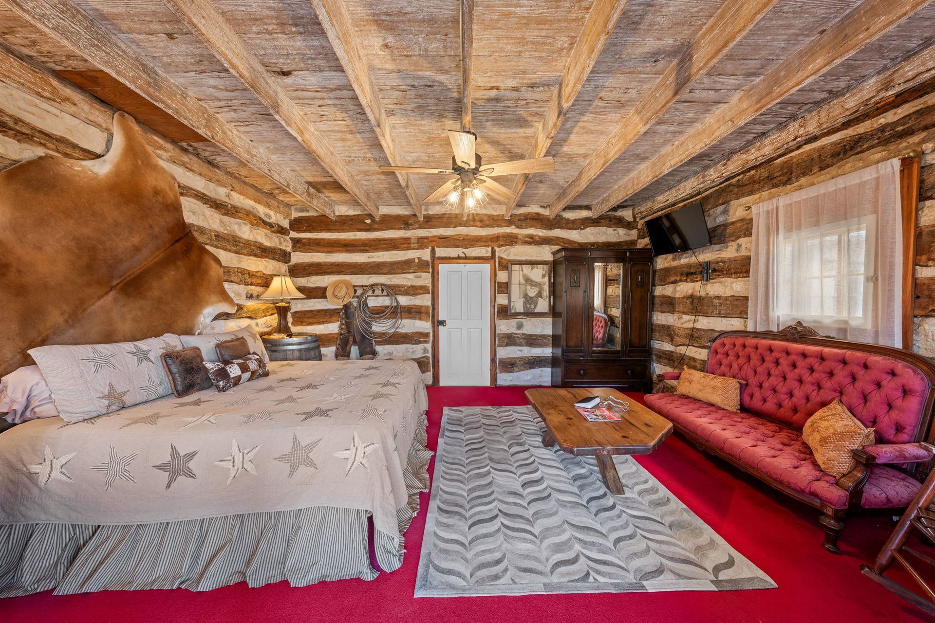 Rustic cabin bedroom with patterned bed, red sofa, wooden walls and ceiling, and red carpet