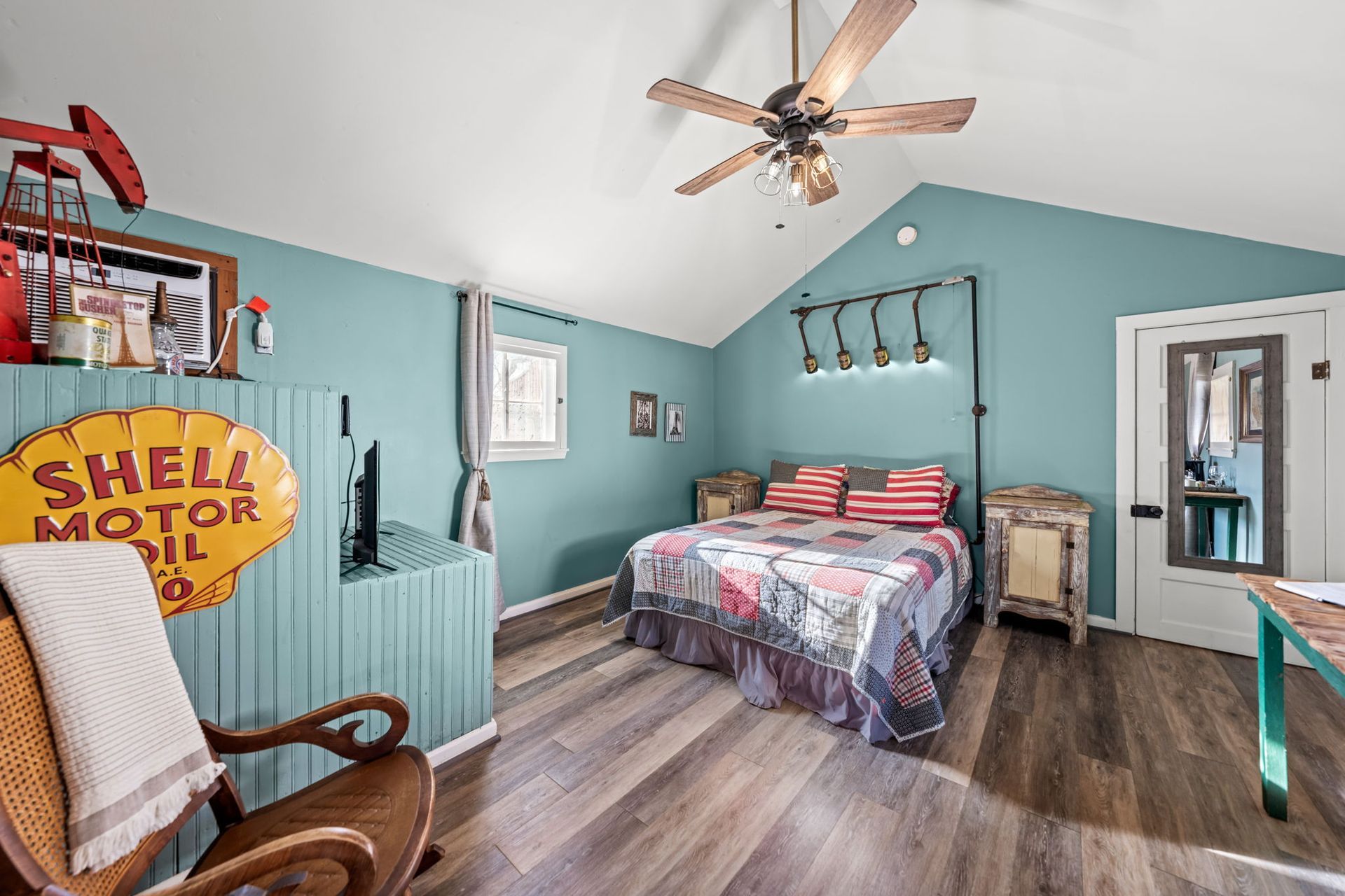 Cozy bedroom with teal walls, a bed, ceiling fan, rocking chair, and vintage Shell Motor sign.