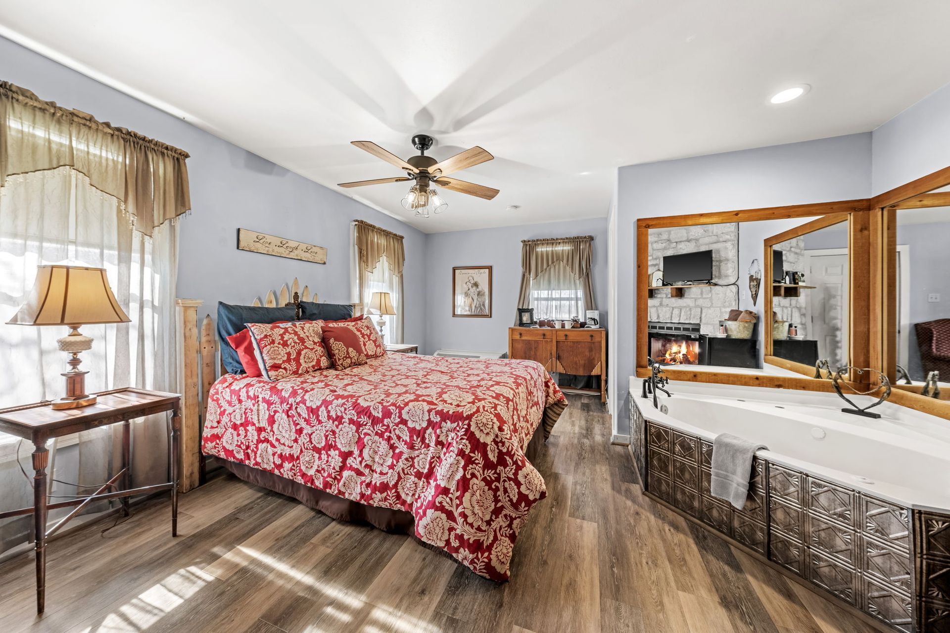 Bright bedroom with a pink floral bedspread, wooden floors, ceiling fan, and mirrored dresser.