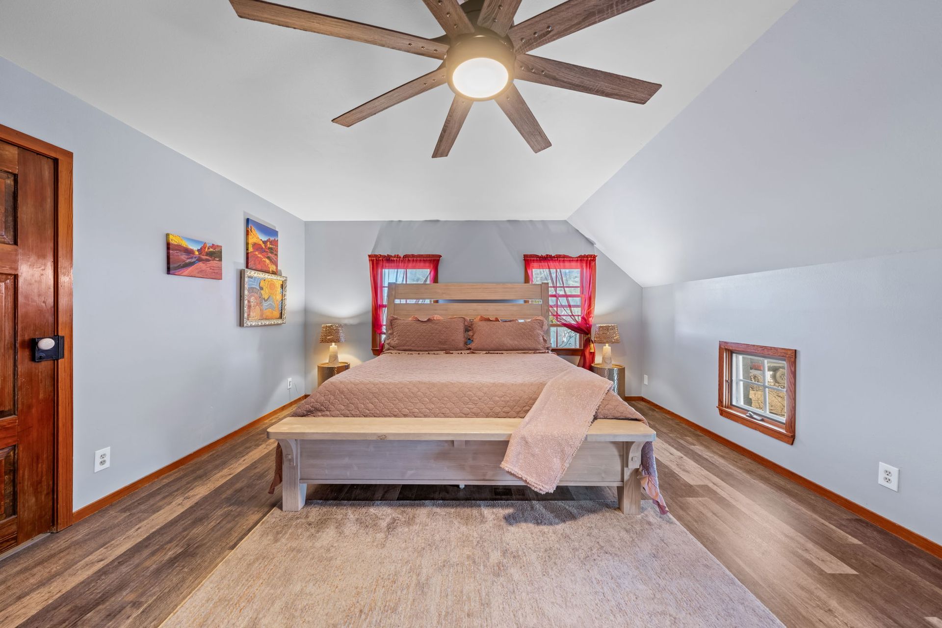 Bedroom with beige bedspread, sloped ceiling, ceiling fan, and red window trim