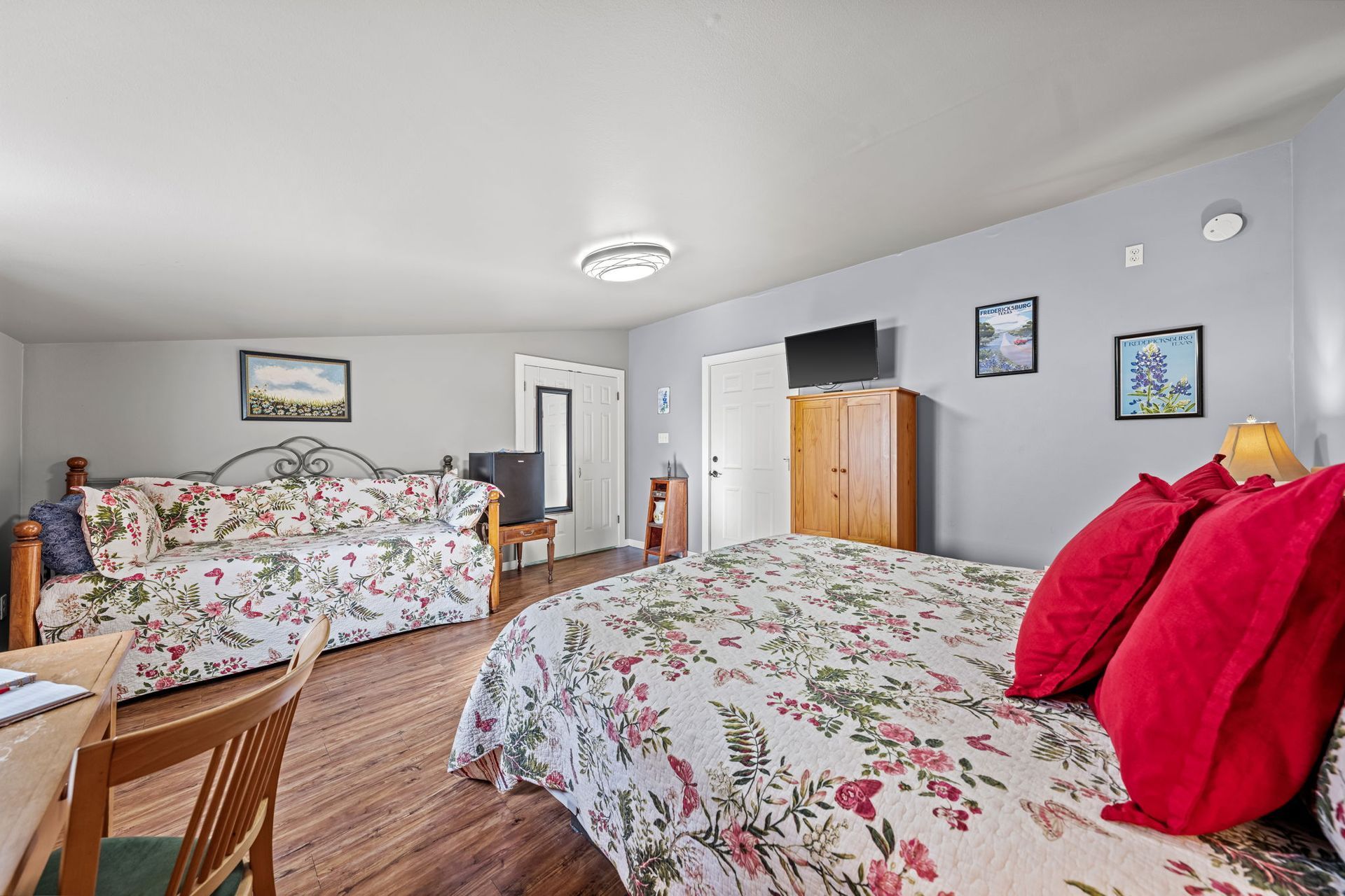 Bright bedroom with two floral beds, wood floor, gray walls, and a dresser near the door.