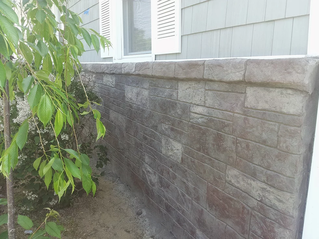 a brick wall next to a house with a tree in front of it .
