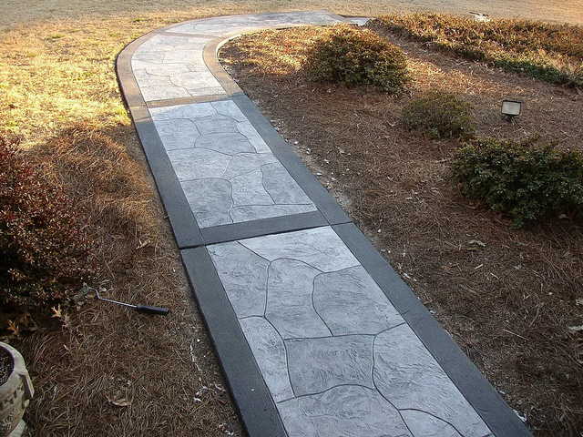a concrete walkway with a black border is surrounded by grass and bushes .