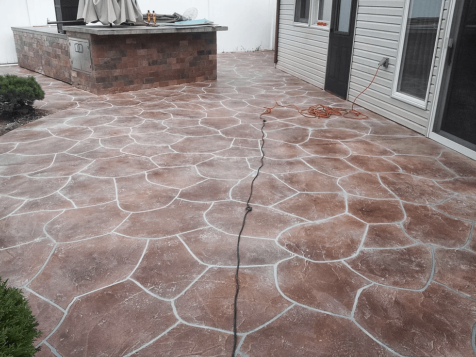 a patio with a stenciled pattern and a grill in the background .