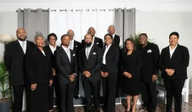 Group of people in black suits posing indoors in front of gray curtains