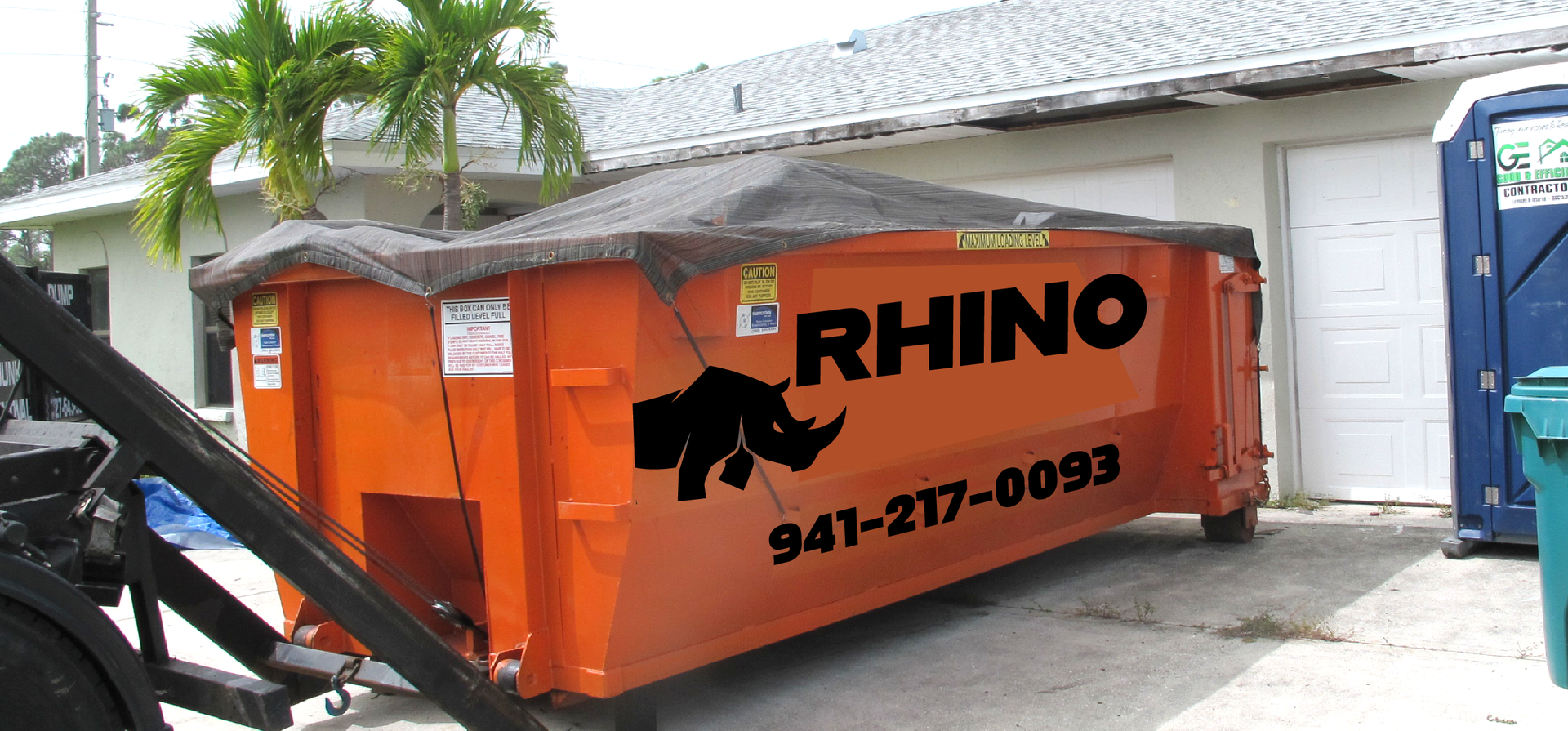 A commercial excavator is moving a large orange dumpsters.