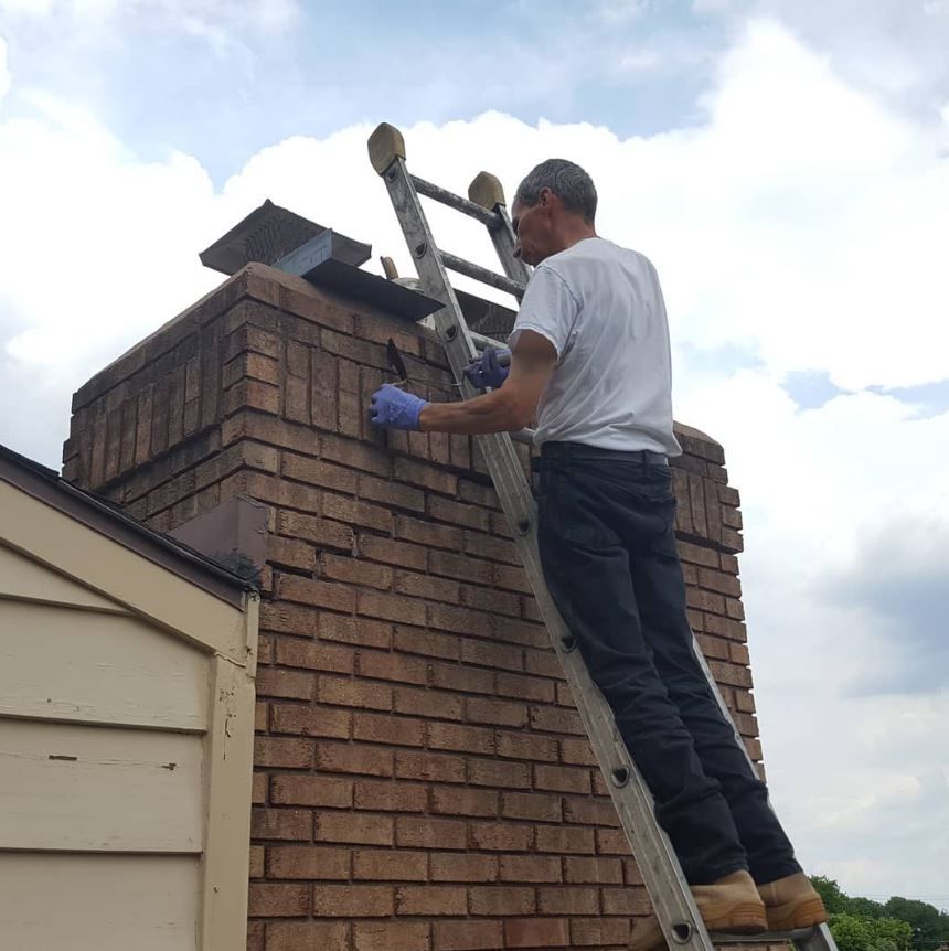 A man standing on a ladder on top of a brick chimney