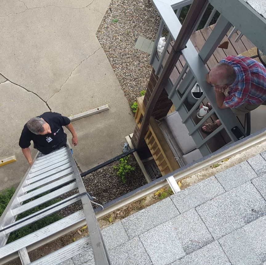 A man on a ladder looking down at another man on a porch